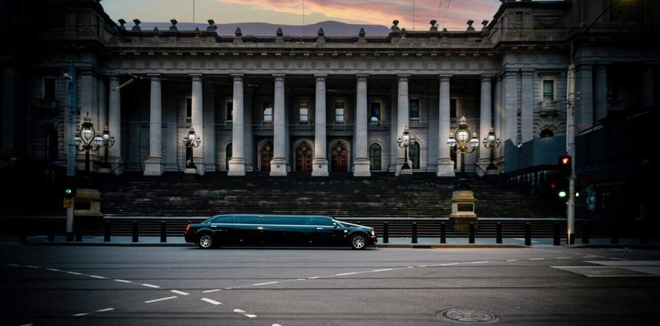 Luxury limousine parked in front of historic government building at dusk.
