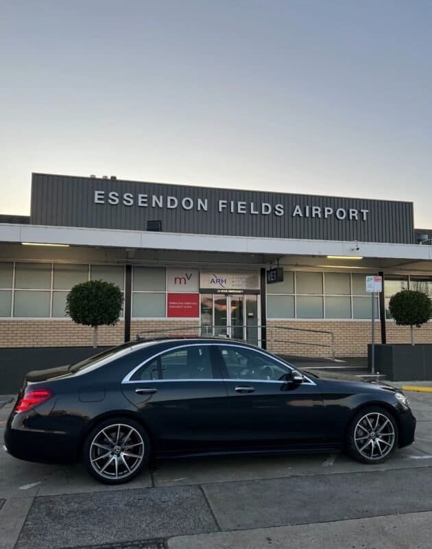 Luxury black car parked outside Essendon Fields Airport terminal.