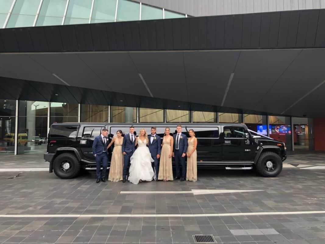 Luxury black limousine with wedding party outside modern building.