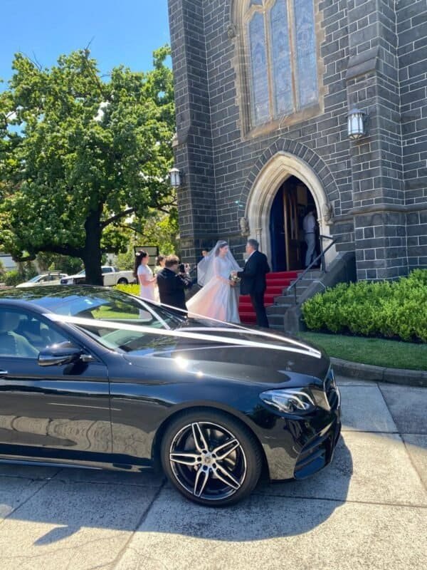 Luxury black car parked outside church for wedding ceremony.
