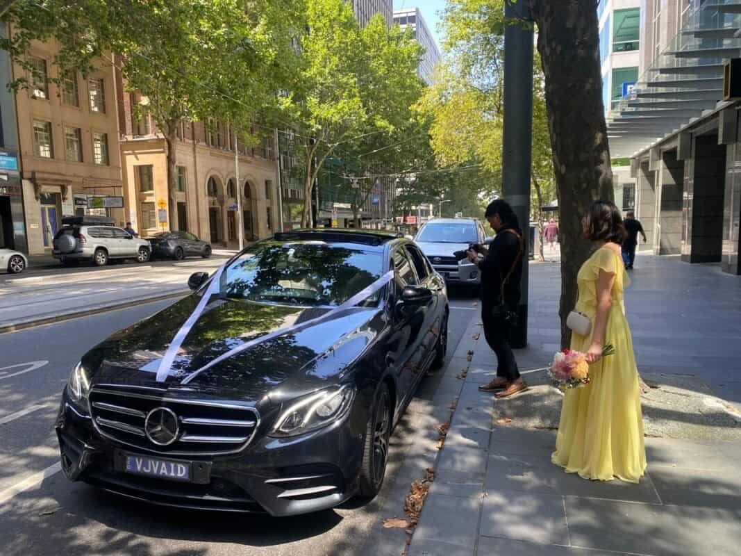 Luxury Mercedes-Benz wedding car with white ribbon on city street.