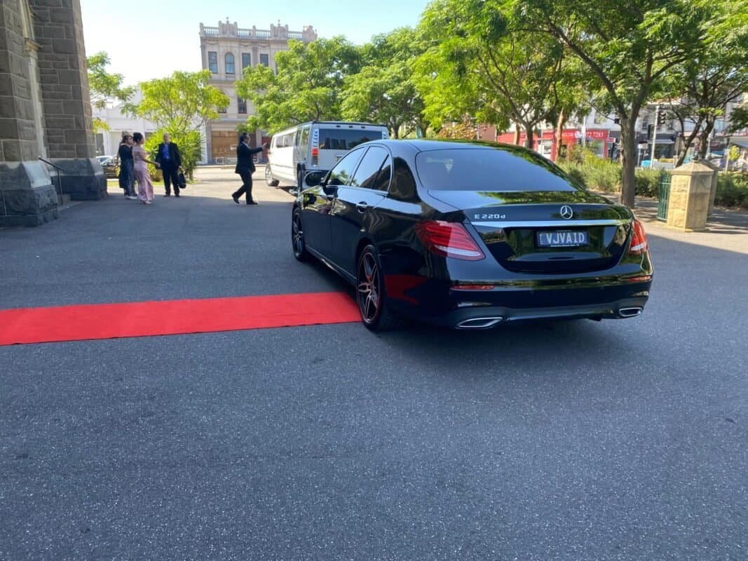 Black Mercedes-Benz E-Class parked outside with people in the background.