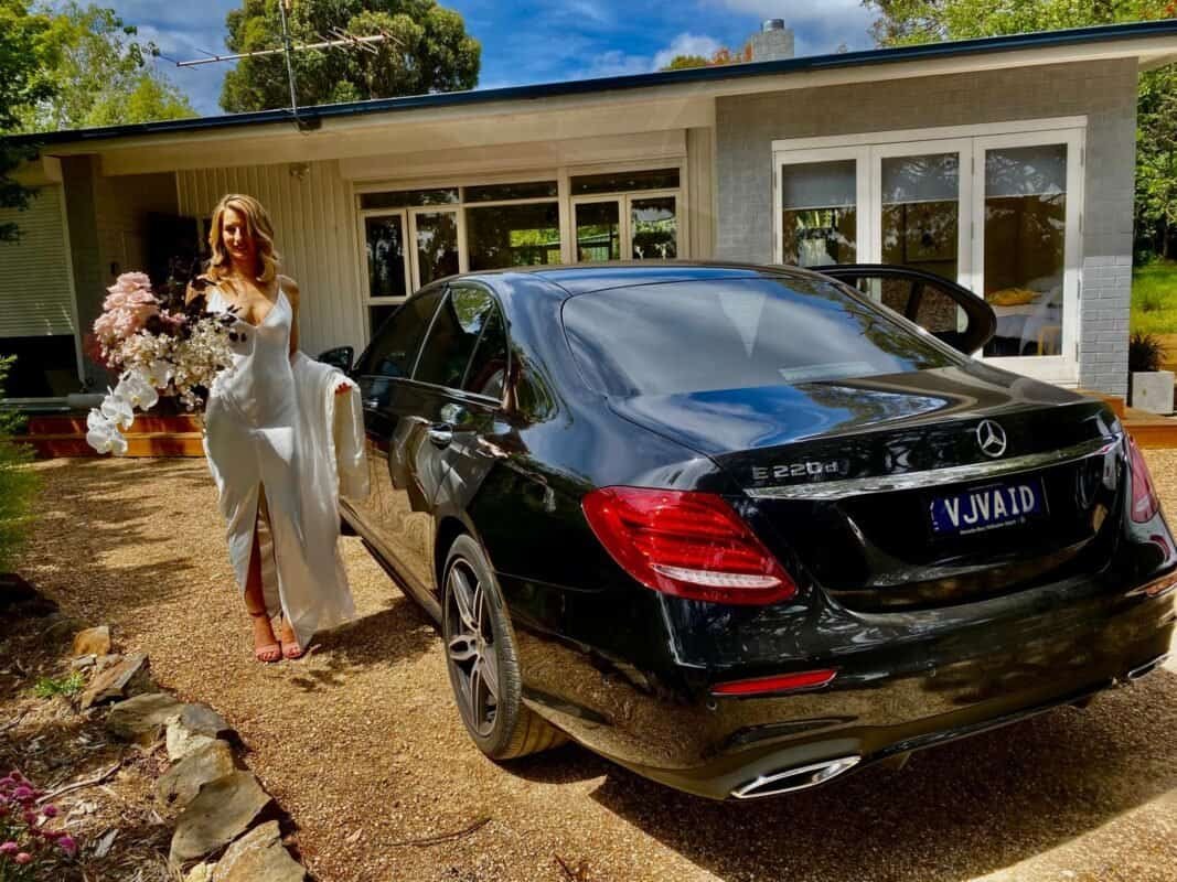 Luxury Mercedes-Benz E220d outside house, woman with flowers, elegant lifestyle.